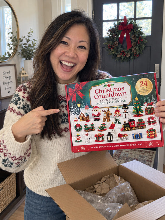 Smiling woman in a holiday sweater pointing to the countdown calendar by the door.